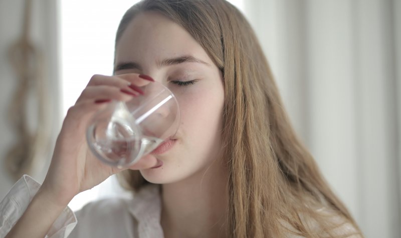 Un mujer bebe agua en su casa para mantener una buena hidratación