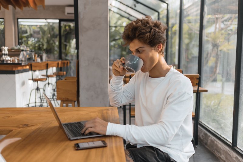 Un hombre joven bebe café mientras trabaja con su laptop en una cafetería