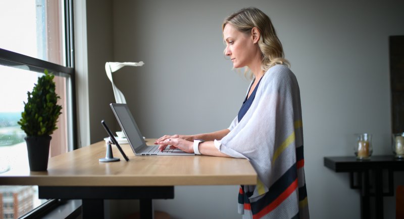 Una mujer que hace teletrabajo escribe en el ordenador portátil que está en un escritorio ajustable