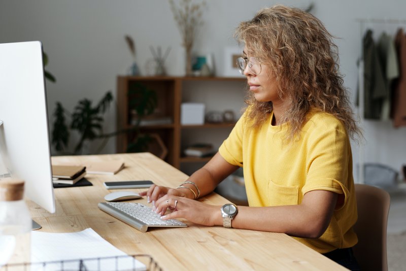 Una mujer que trabaja desde casa con el ordenador en un entorno de trabajo con todo lo necesario, que es uno de los factores que influyen en la productividad laboral