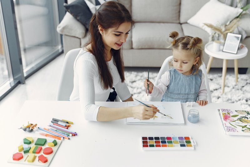 Una madre que hace teletrabajo en casa toma un descanso para pintar con acuarelas con su hija