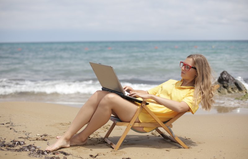 Una mujer trabaja con el ordenador portátil estirada en una silla en la playa