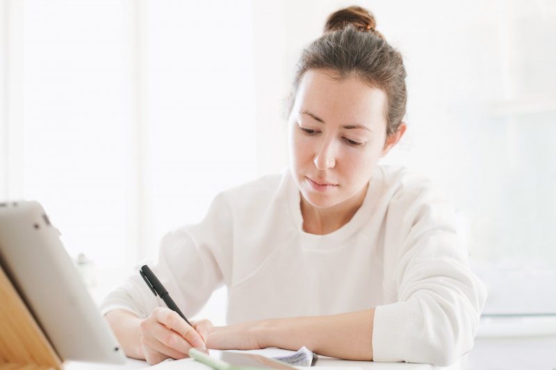 Una mujer escribe en una libreta las tareas a realizar durante el día siguiendo las directrices de método Debo, Debería, Quiero