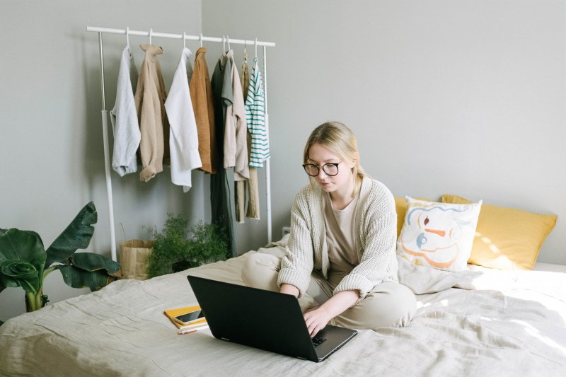 Una mujer está en el dormitorio de su casa y usa su ordenador portátil en la cama para trabajar