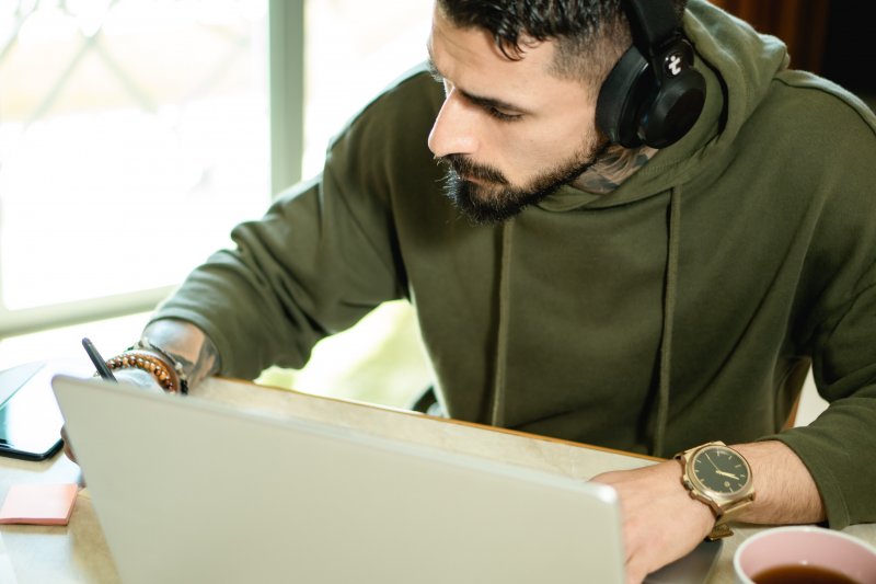 Un hombre escucha música lo-fi para concentrarse mientras trabaja en casa con el ordenador portátil