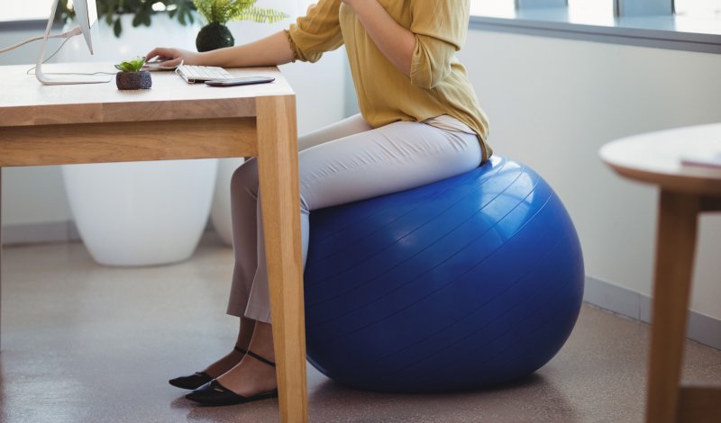 Mujer trabaja con el ordenador sentada en una pelota de Pilates en su oficina en casa