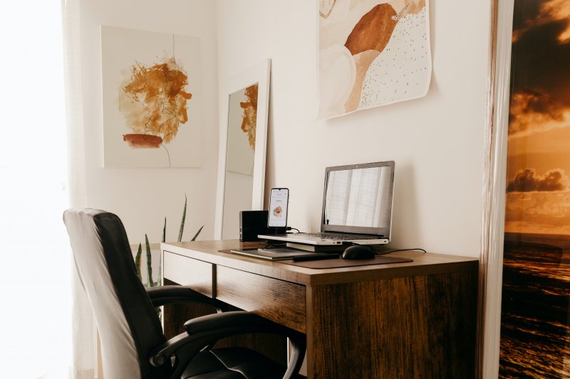 Silla con apoyabrazos ante una mesa con un ordenador portátil y un teléfono móvil en una oficina en casa