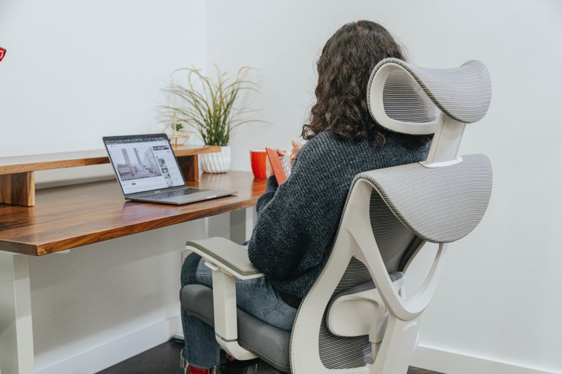 Una teletrabajadora está sentada en una silla de oficina con reposacabezas mientras trabaja con el ordenador portátil en su oficina en casa