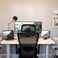 Un espacio de trabajo en casa con una silla ergonómica de respaldo alto y tres monitores