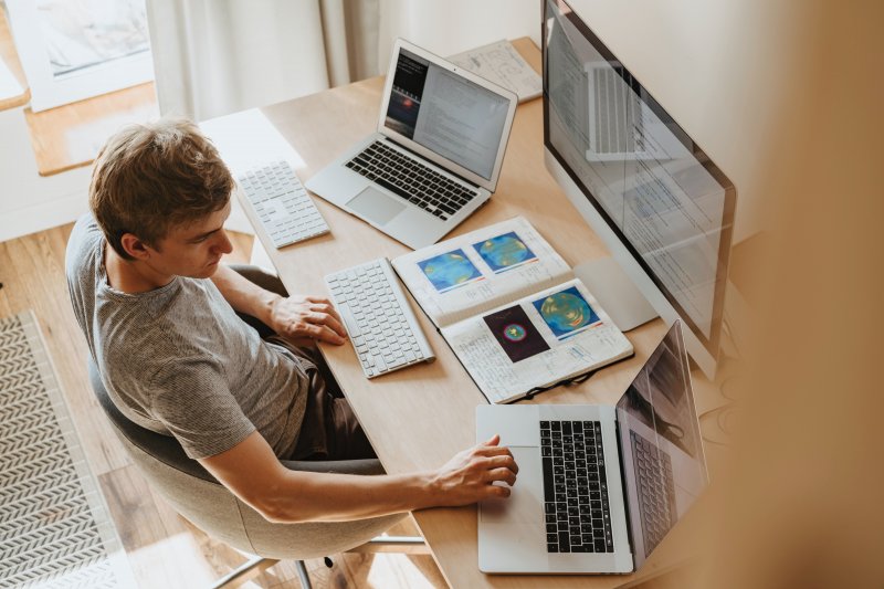 Un hombre trabaja desde casa con diferentes ordenadores y prueba varias técnicas de productividad para mejorar su rendimiento laboral