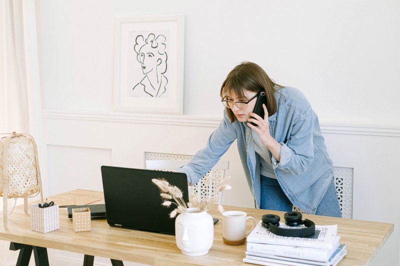 Una mujer parece tecnoestrés y trabaja al mismo tiempo con el ordenador portátil mientras que atiende una llamada al teléfono móvil