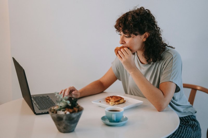 Una mujer que trabaja en casa se prepara una comida y la ingiere ante el ordenador portátil