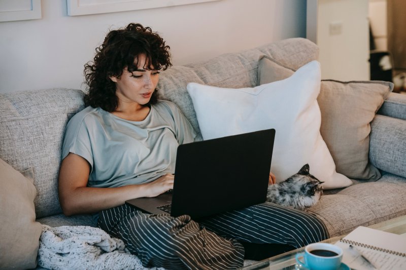Una mujer que hace teletrabajo escribe en pijama en el ordenador portátil que está en su regazo