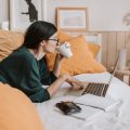 Una mujer trabaja en la cama con su ordenador portátil y bebe café en una taza